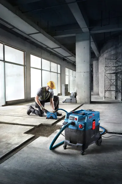 A person wearing safety equipment operates an all-purpose extractor on a concrete floor.