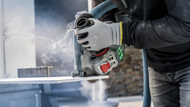 A person wearing safety equipment uses a power cutter to cut a stone slab.
