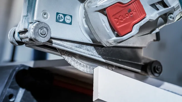 Circular saw cutting a white tile with a safety warning label visible.