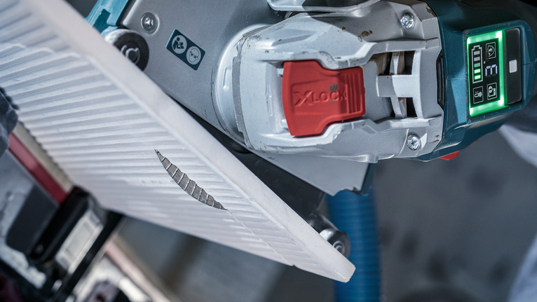 Angle grinder cuts through a ceramic tile along a marked line.