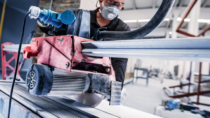 A person wearing safety equipment cuts metal pipes with a large circular saw.