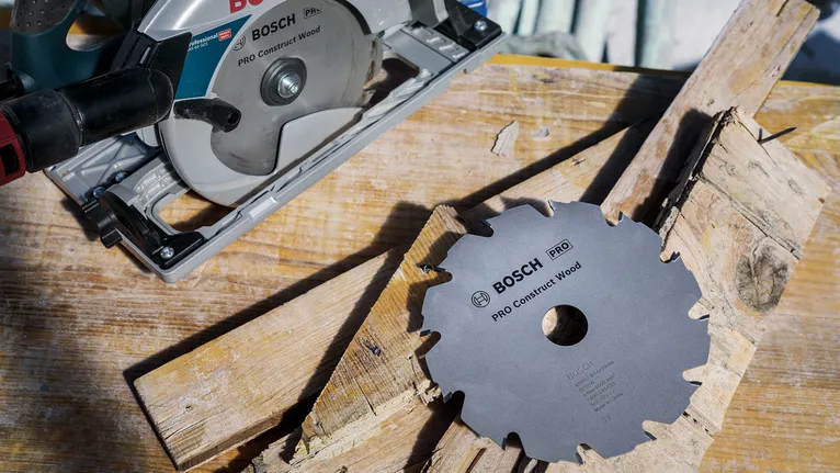 Circular saw and separate saw blade placed on wooden planks.