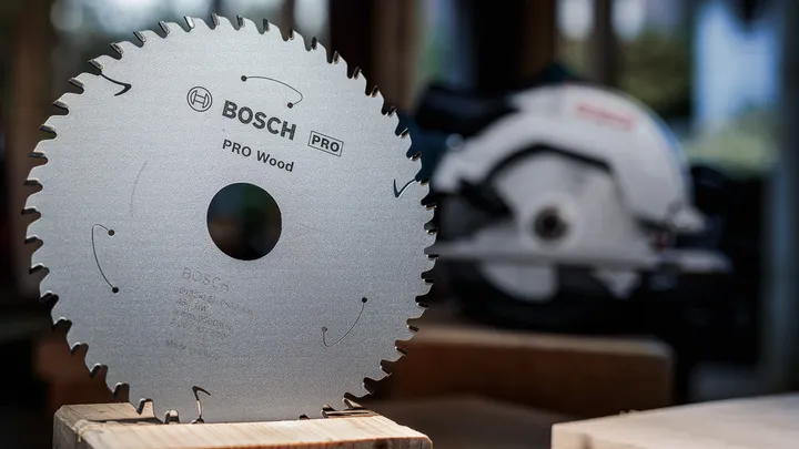 Circular saw blade displayed upright on wood with a power saw in the background.
