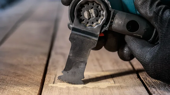 Person wearing safety equipment using a multi-tool to cut wood.