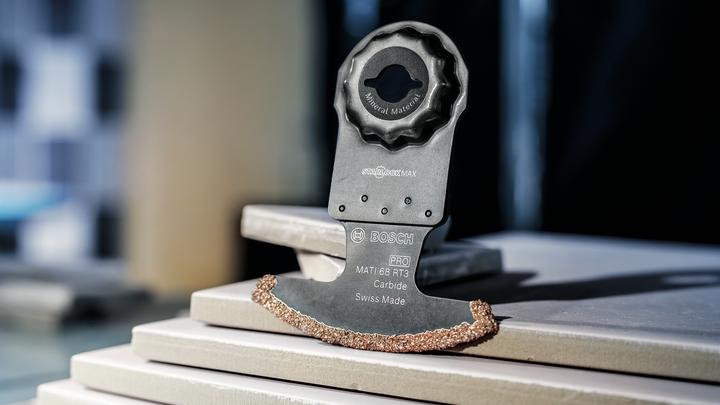 Oscillating tool blade with carbide edge rests on stacked ceramic tiles.