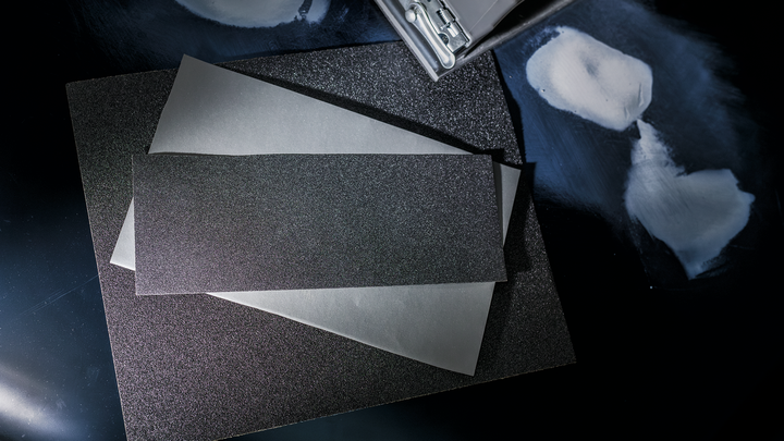 Sheets of sandpaper stacked on a dark surface next to areas prepared for sanding.