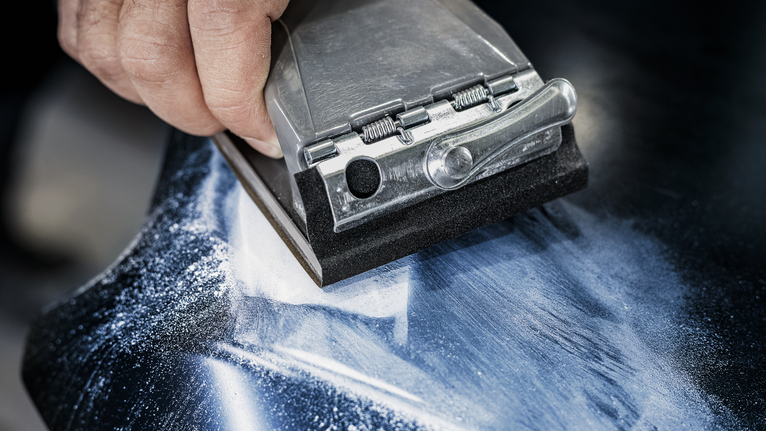 Person using a hand sander to smooth a surface covered in dust.