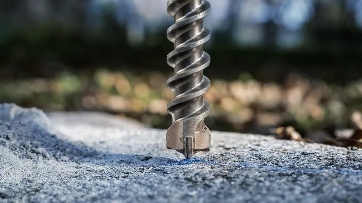Large masonry drill bit boring into concrete outdoors.