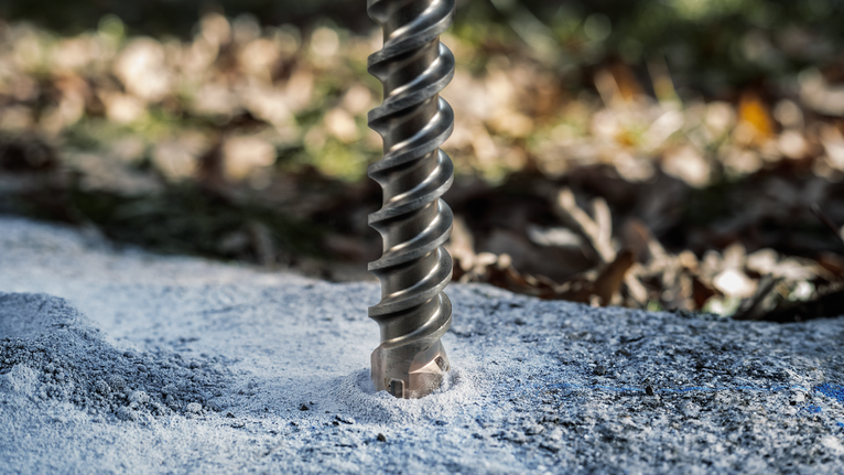 Large drill bit creating a hole in concrete outdoors.