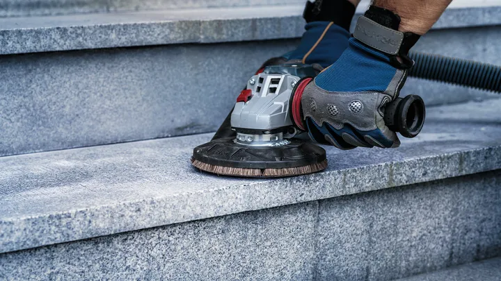 A person wearing safety equipment polishes stone stairs with a power tool.