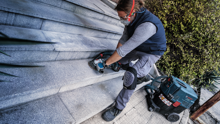 Person wearing safety equipment grinds stone steps with an electric tool.