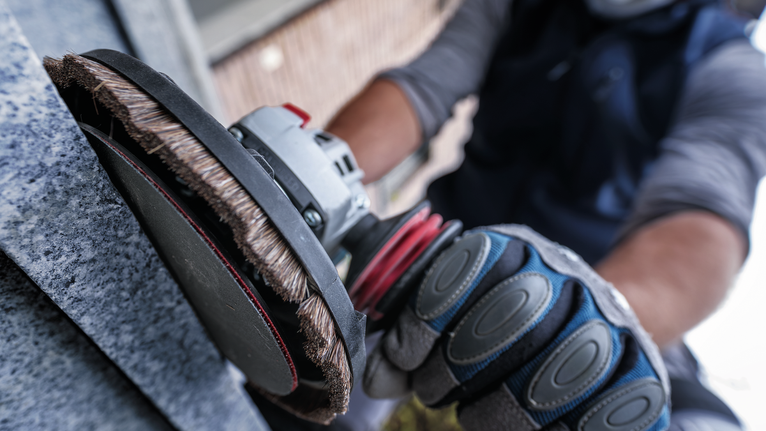 Person wearing safety equipment polishes a stone surface with a rotary tool.