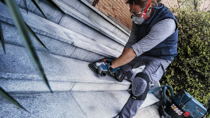 Person wearing safety equipment grinds stone stairs with a power tool.