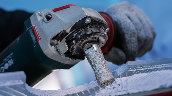 Person wearing safety equipment grinds stone with a rotary power tool.