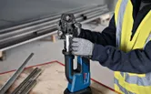 A person wearing safety equipment uses a cordless press tool at a workbench.