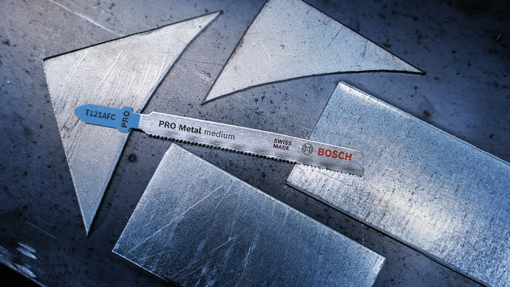 Jigsaw blade placed on a metal sheet with several cut metal pieces.
