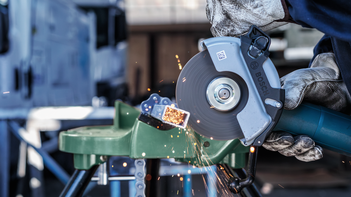 Person wearing safety equipment uses an angle grinder to cut metal, producing sparks.