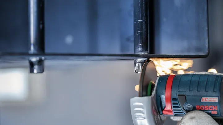 Person wearing safety equipment grinds metal, creating sparks.