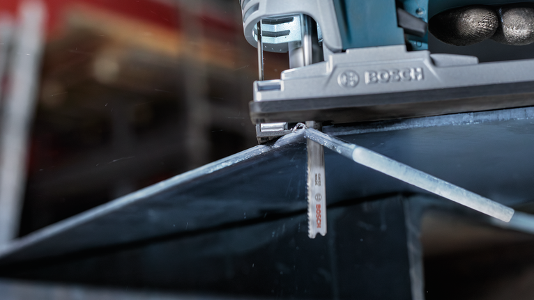 Jigsaw cutting through a metal sheet along a marked line.