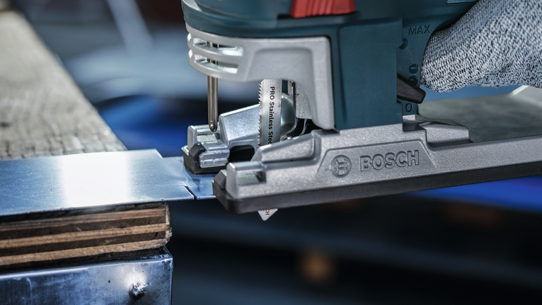 Person wearing safety equipment cuts metal sheet with a jigsaw.