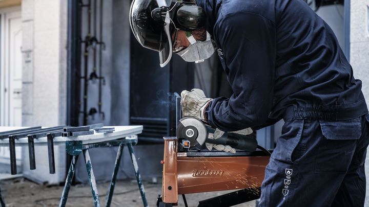 A person wearing safety equipment grinds metal, producing sparks.