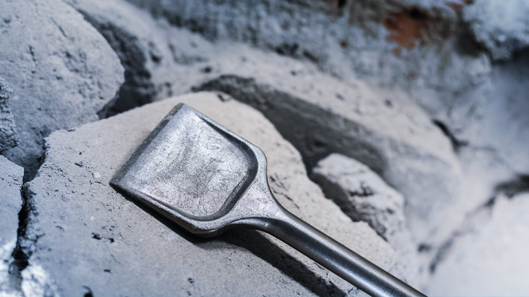 Wide chisel resting on broken concrete rubble.