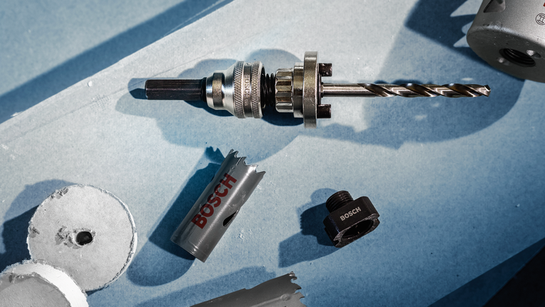 Metal drill bit with hole saw attachments and cut discs on a blue surface.