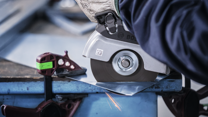 Person wearing safety equipment cuts sheet metal with a circular saw, producing sparks.