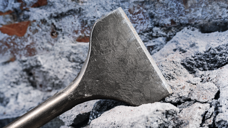 Wide chisel breaks through concrete debris at a demolition site.