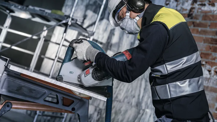 Person wearing safety equipment cuts tile with a circular saw on a construction site.