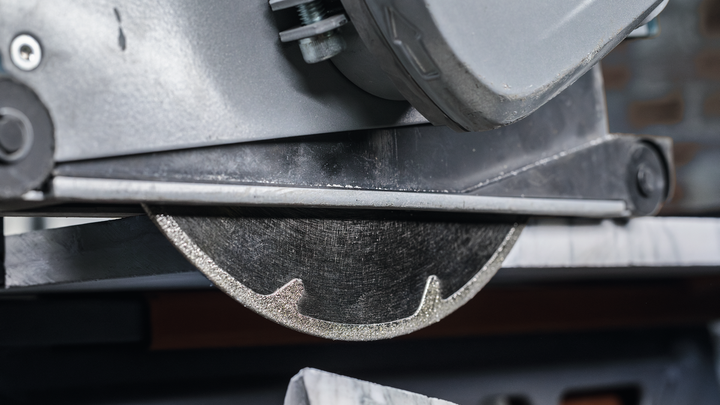Diamond saw blade cutting a piece of tile in a workshop.