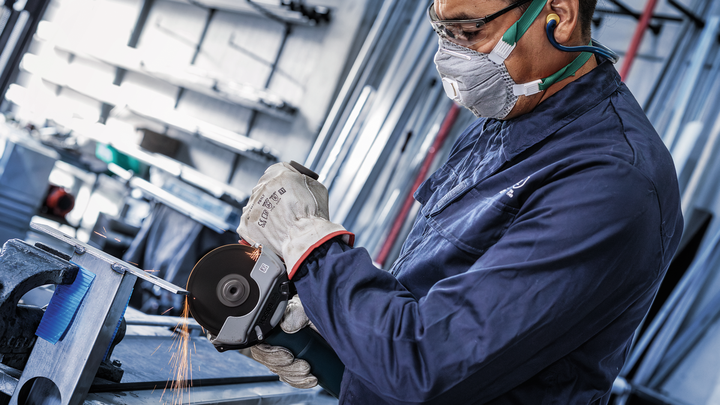 A person wearing safety equipment grinds metal, producing sparks.