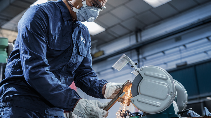 Person wearing safety equipment uses a metal cutting saw to cut a pipe, producing sparks.