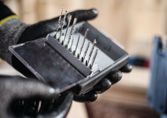 Person wearing safety equipment holding a case of assorted drill bits.