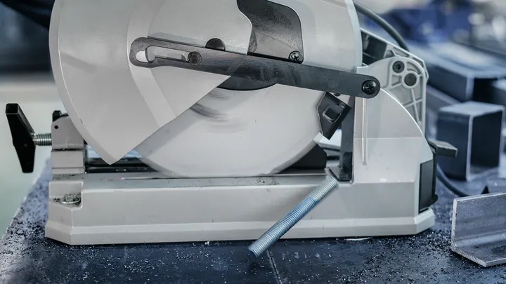 Metal cutting saw slicing through a steel rod in a workshop.