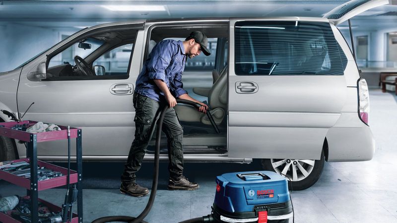 A person wearing safety equipment uses a wet dry extractor to clean a car interior.