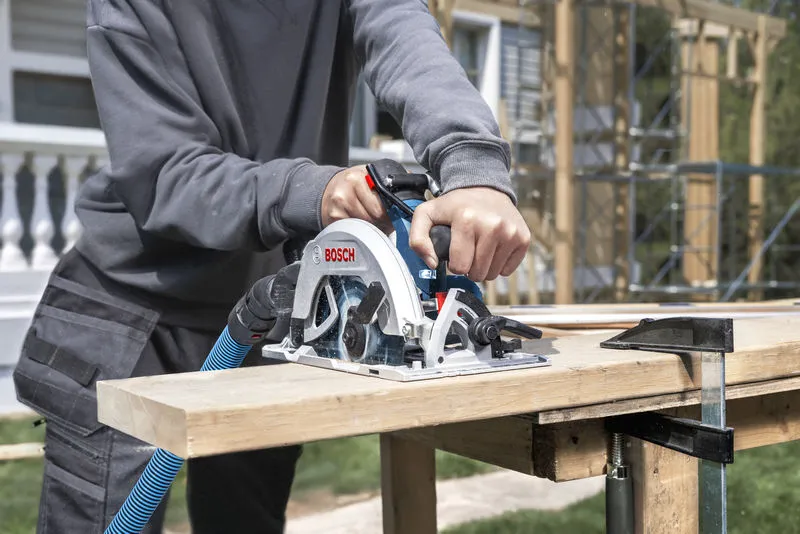 A person cuts a wooden board with a cordless circular saw at a construction site.