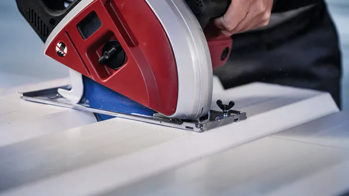 Person guides a circular saw to cut a white board.