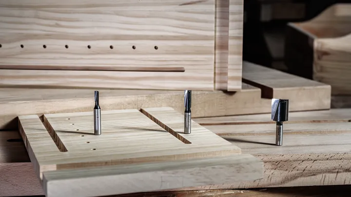 Router bits placed on a wooden board with freshly cut grooves in a carpentry workshop.