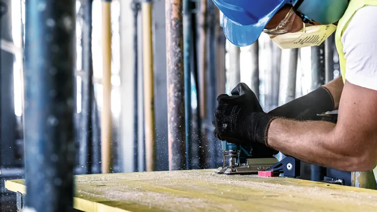 Person wearing safety equipment uses a power tool to cut wood.