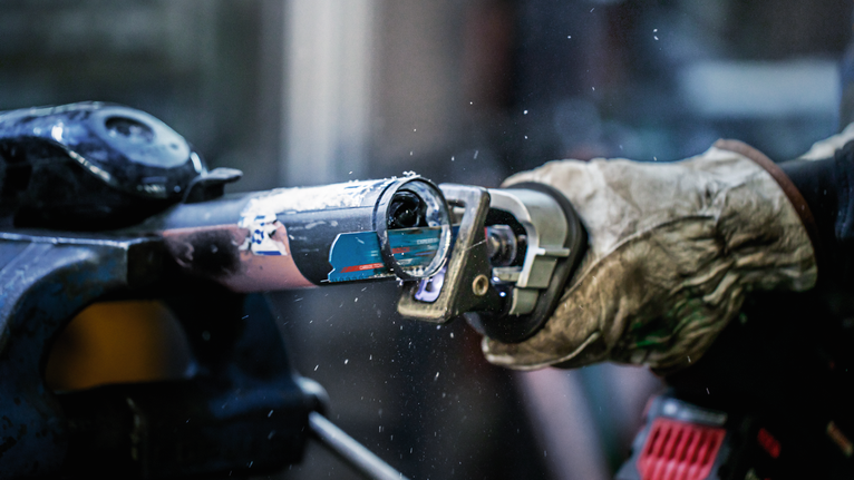 Person wearing safety equipment cuts a metal pipe with a power tool.