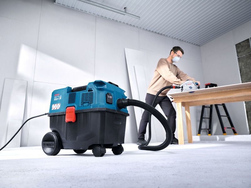A person wearing safety equipment uses an all-purpose extractor while cutting wood on a table.