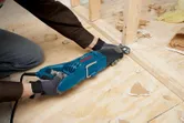 A person wearing safety equipment uses a reciprocating saw to cut wood framing.