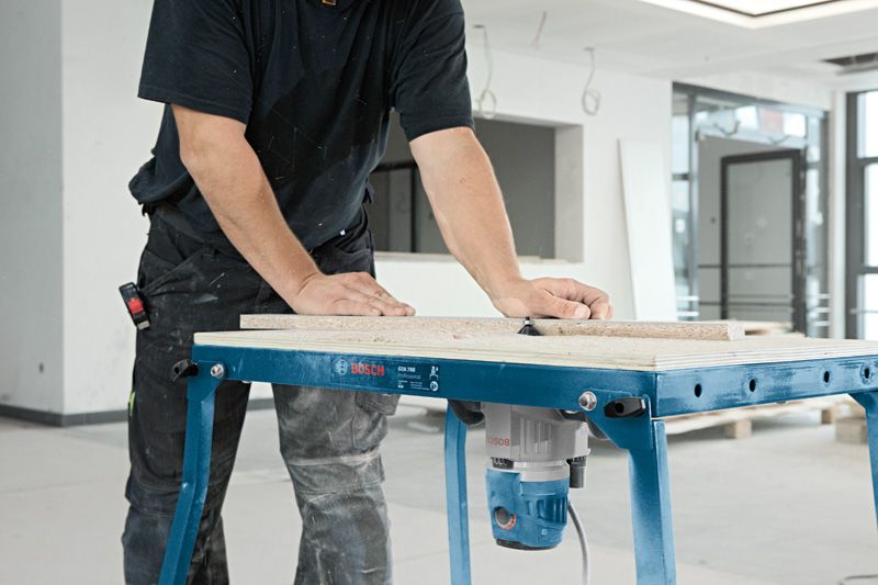 A person guides wood through a multifunction router mounted on a workbench.