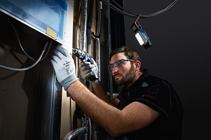Una persona que usa equipo de seguridad perfora una pared y una luz inalámbrica ilumina el espacio de trabajo.