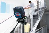 Herramienta de nivelación láser que proyecta líneas a través de una escalera mientras una persona prepara una pared.