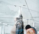 Una persona que usa equipo de seguridad perfora un techo de hormigón.