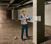 Una persona que usa equipo de seguridad perfora un agujero en un pilar de hormigón.
