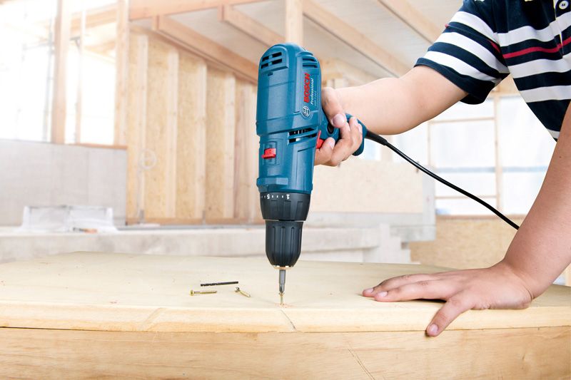 Una persona utiliza un taladro con cable para fijar un tornillo en la madera.
