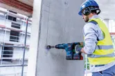 Una persona que usa equipo de seguridad utiliza un martillo perforador inalámbrico para perforar hormigón.
